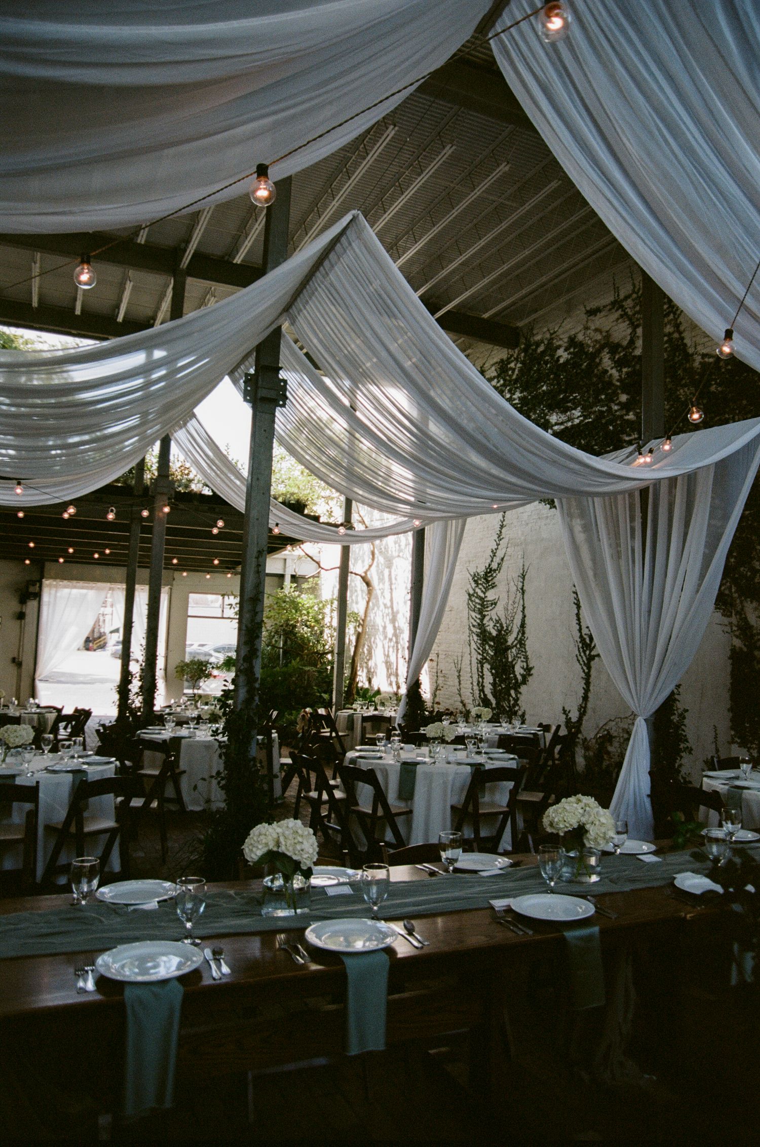 Elegant wedding reception venue with white draped fabric ceiling and romantic string lights creating an ethereal atmosphere.