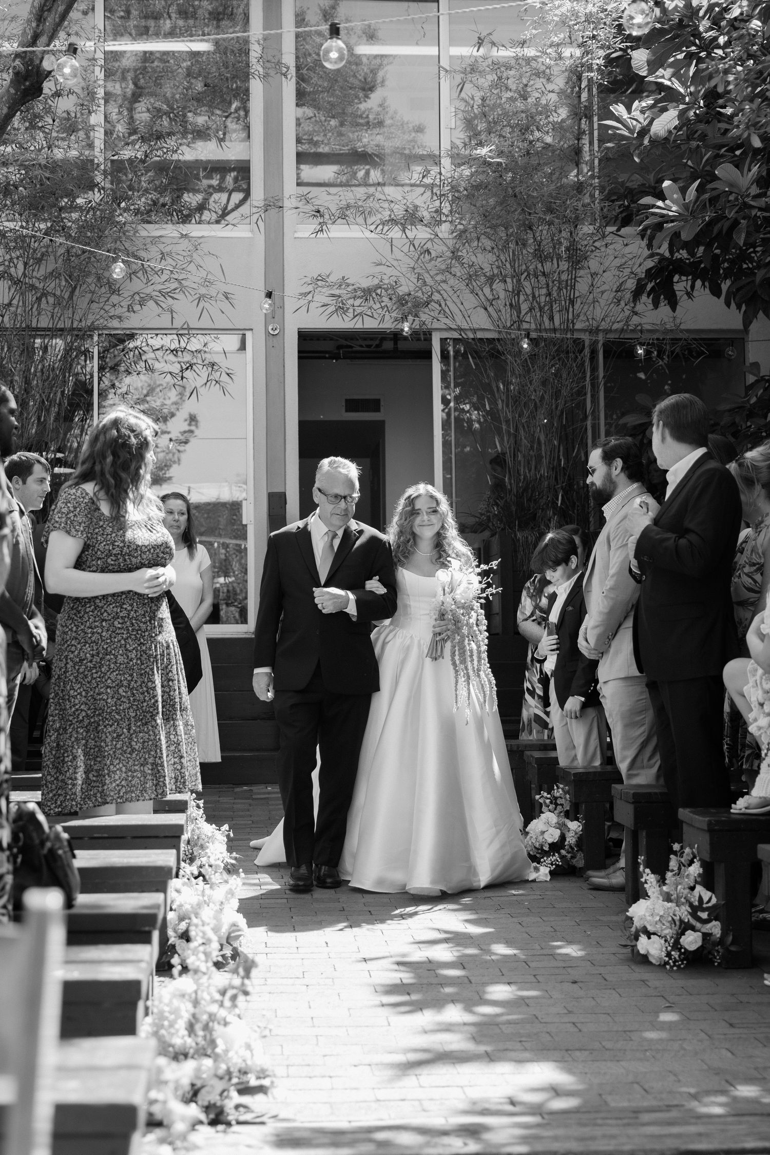 Wedding guests gather in a sunlit courtyard during an elegant outdoor reception celebration.