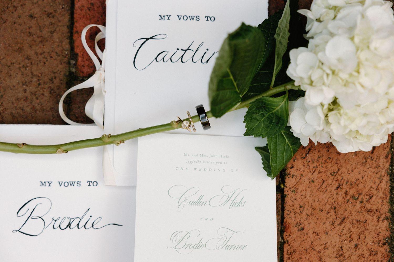 Wedding invitations and white floral decorations arranged on a rustic brown textured surface.
