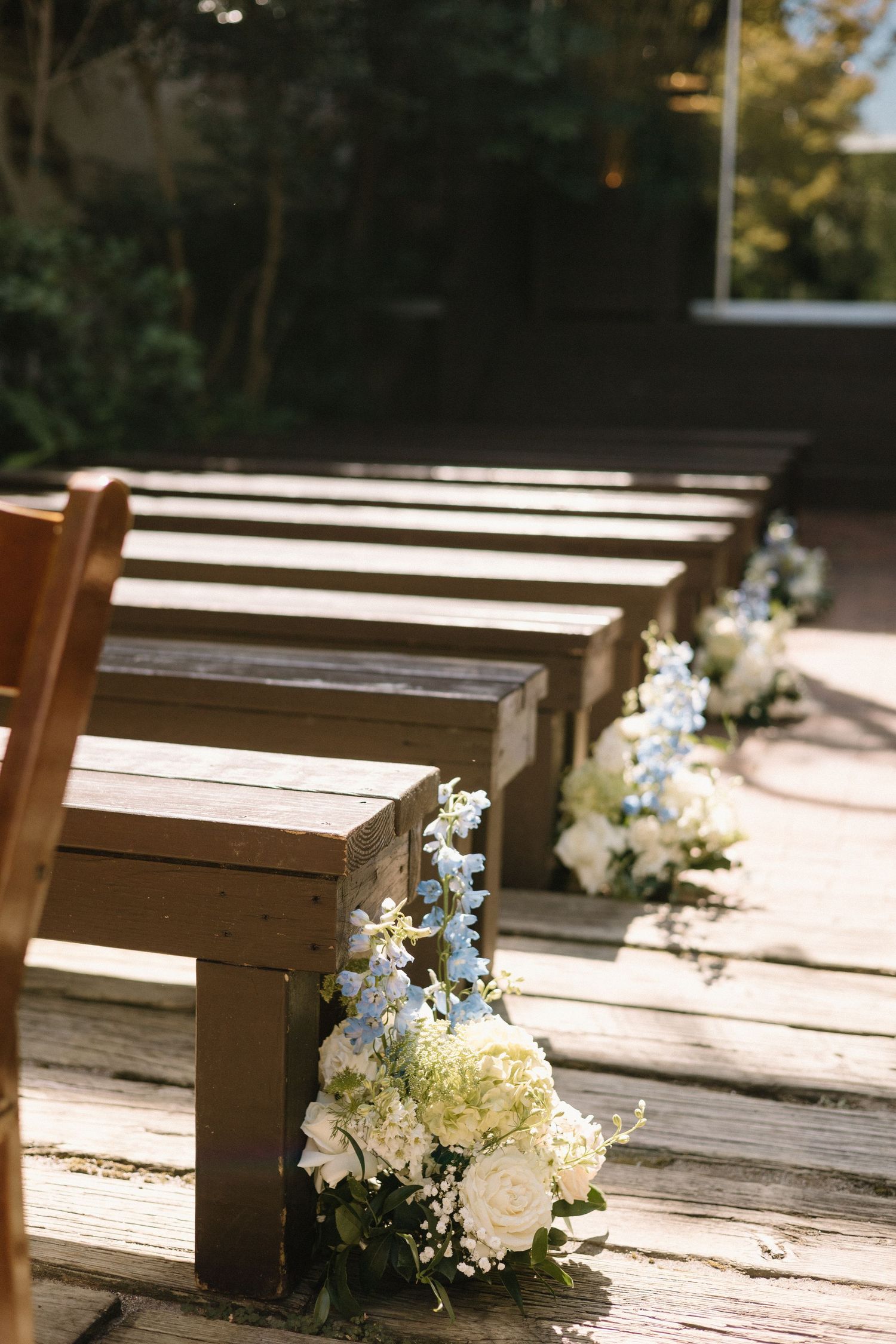 Wooden benches adorned with delicate white and blue floral arrangements line up in rows under natural sunlight.