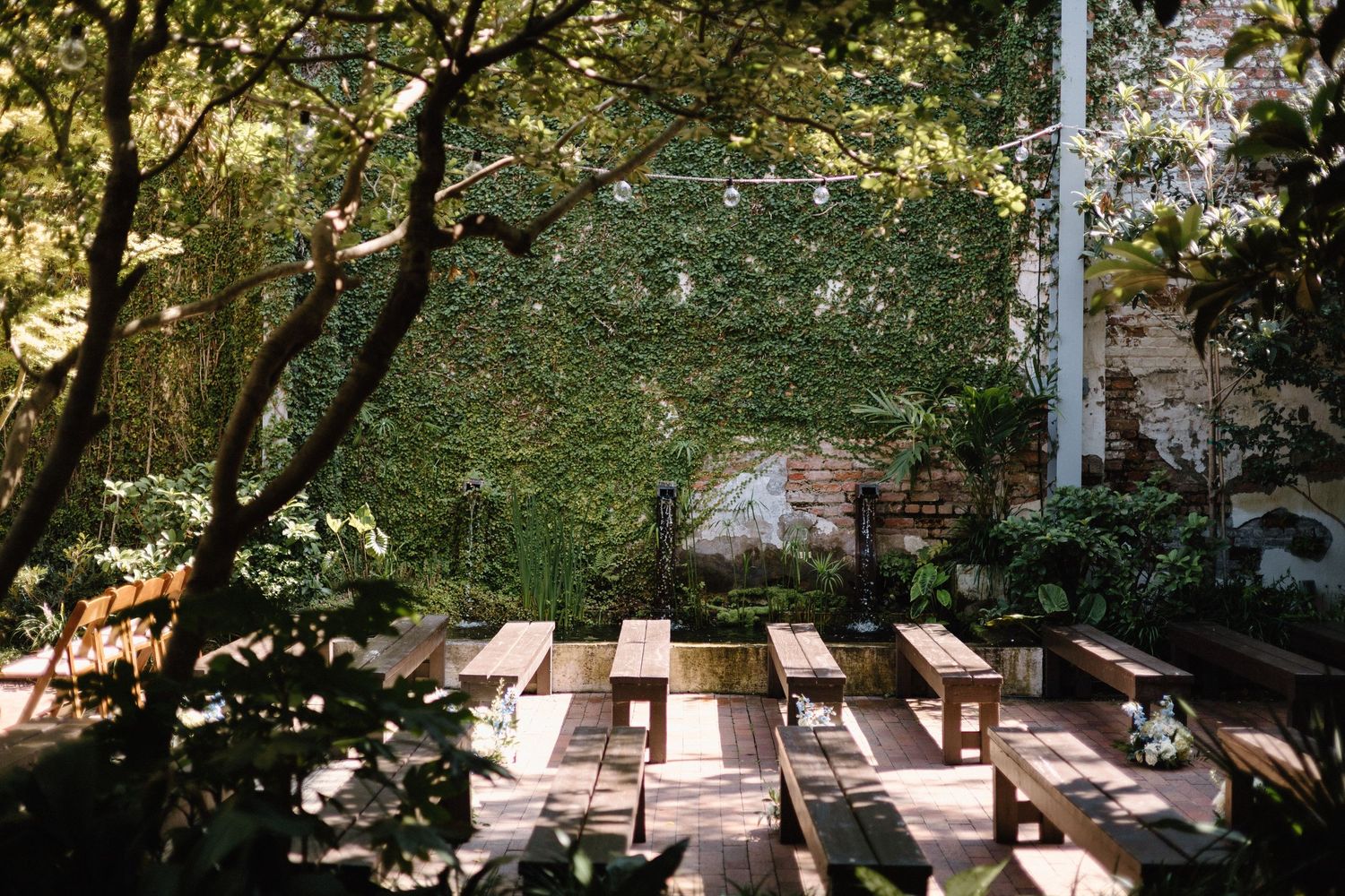 Sunlit wooden picnic tables arranged in rows under shady trees in a peaceful outdoor garden setting.