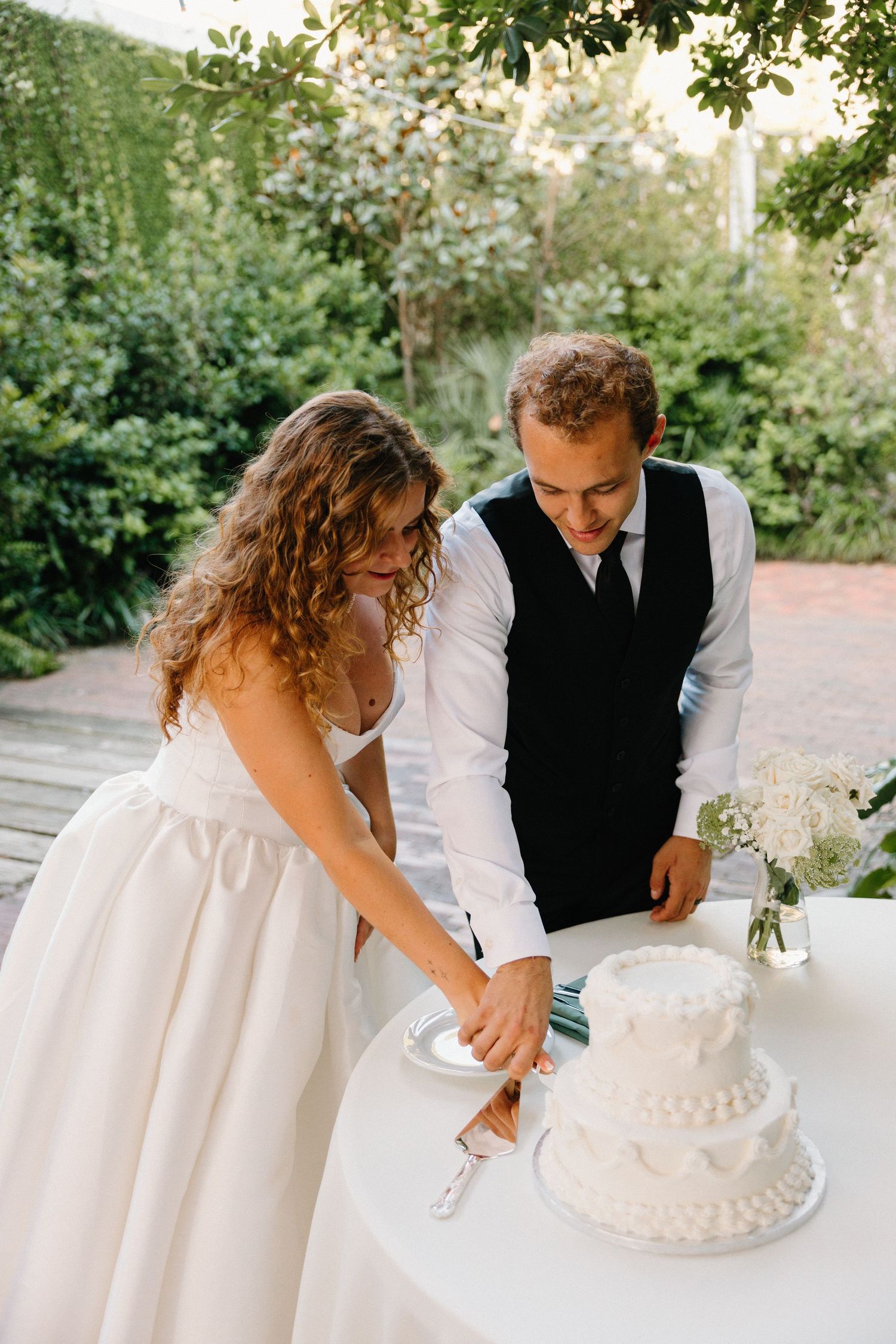 A couple cutting their white wedding cake together during an outdoor reception celebration.
