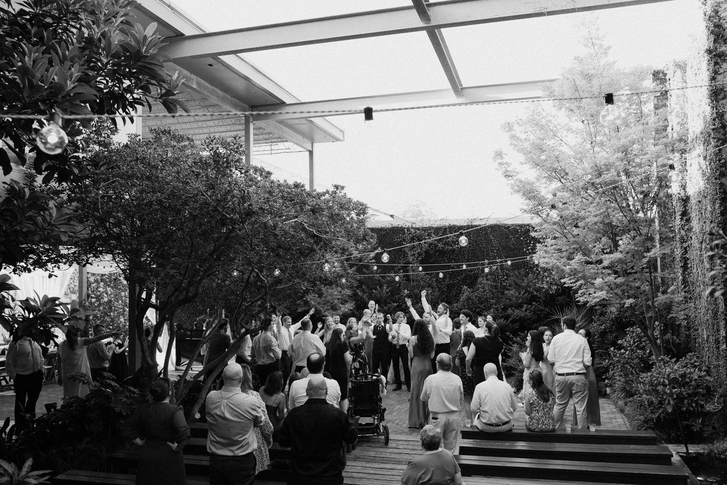 A panoramic view of an outdoor wedding reception setup with white tent and trees in the background.