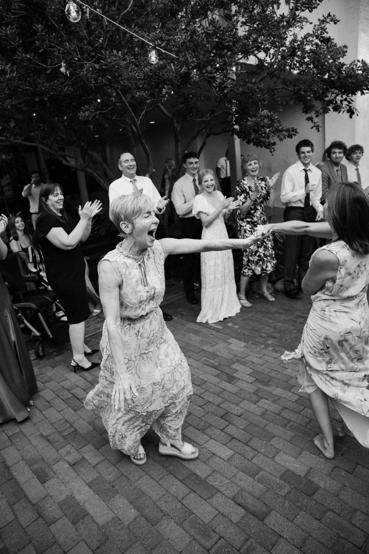 A sequence of black and white photos showing energetic dancing at an outdoor wedding reception on brick pavement.