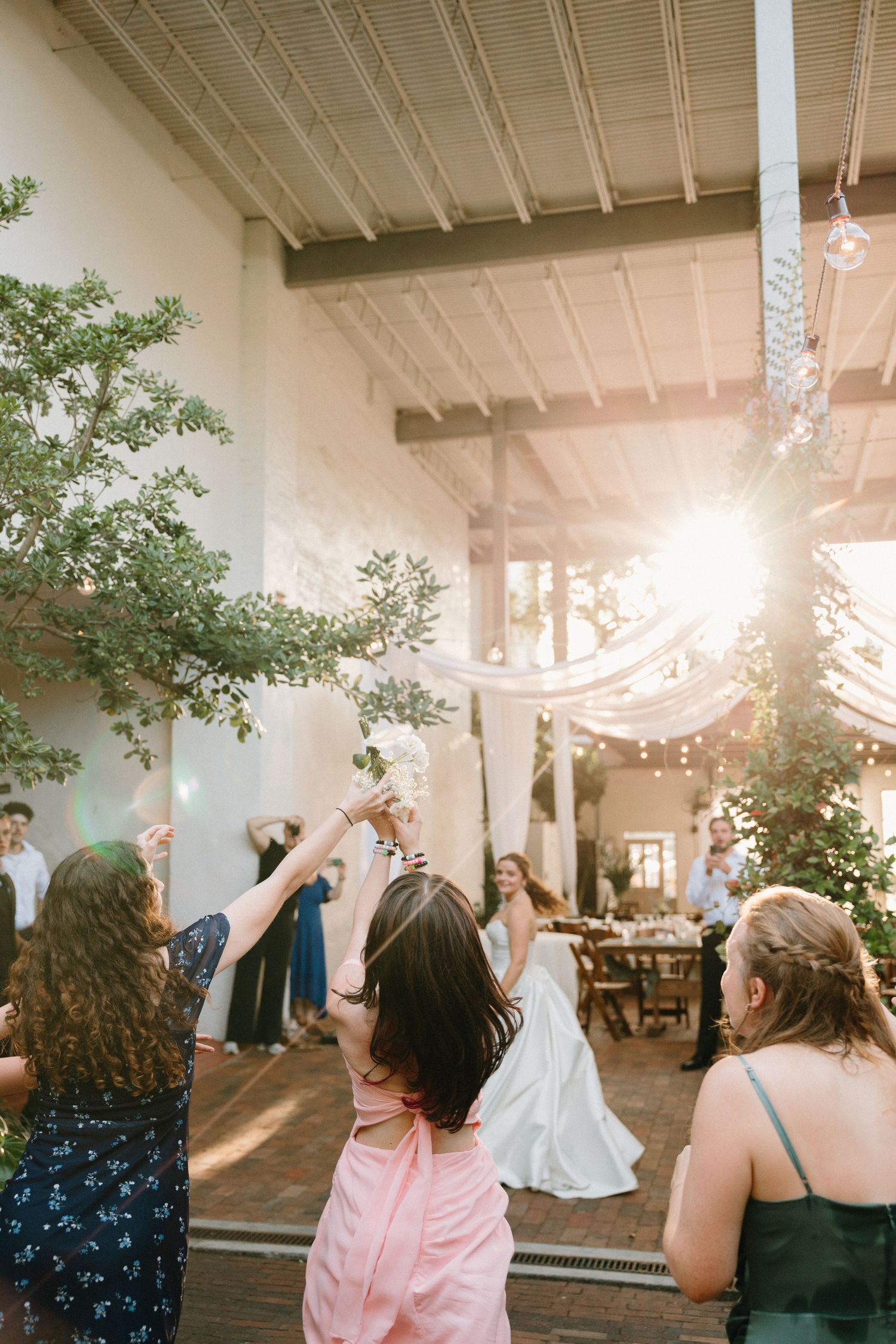Wedding guests dance and celebrate during a reception under twinkling lights in an elegant indoor venue.