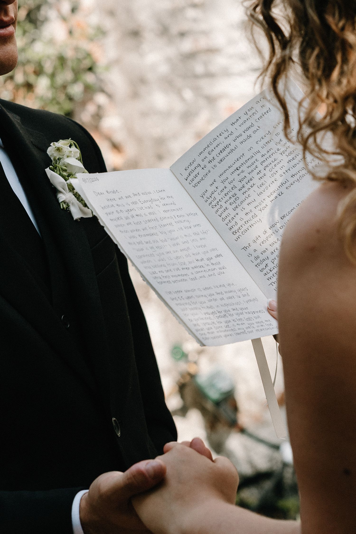 Someone reading handwritten wedding vows from paper during an outdoor ceremony.