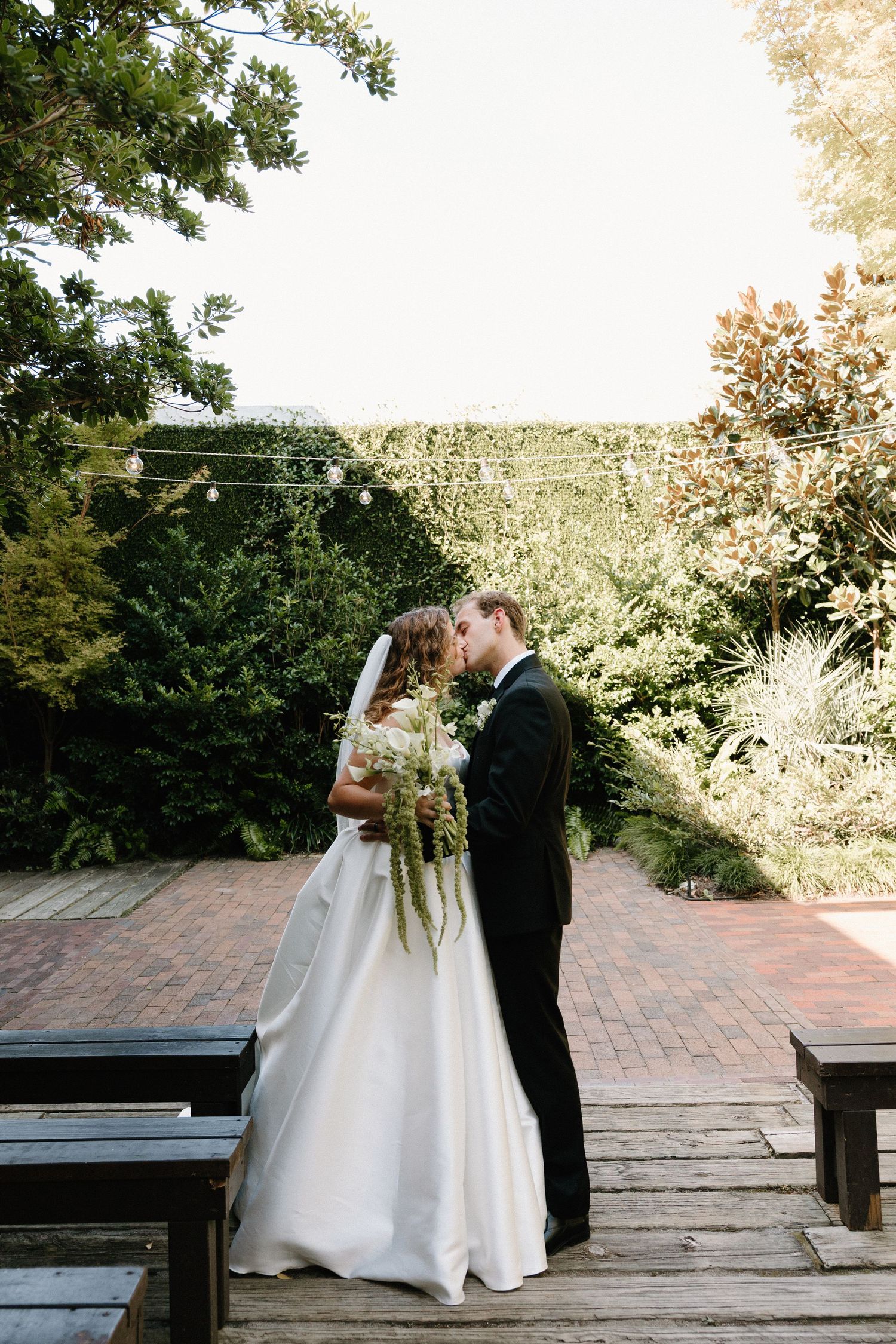 Romantic wedding couple sharing intimate moments on a brick patio surrounded by lush greenery at sunset.