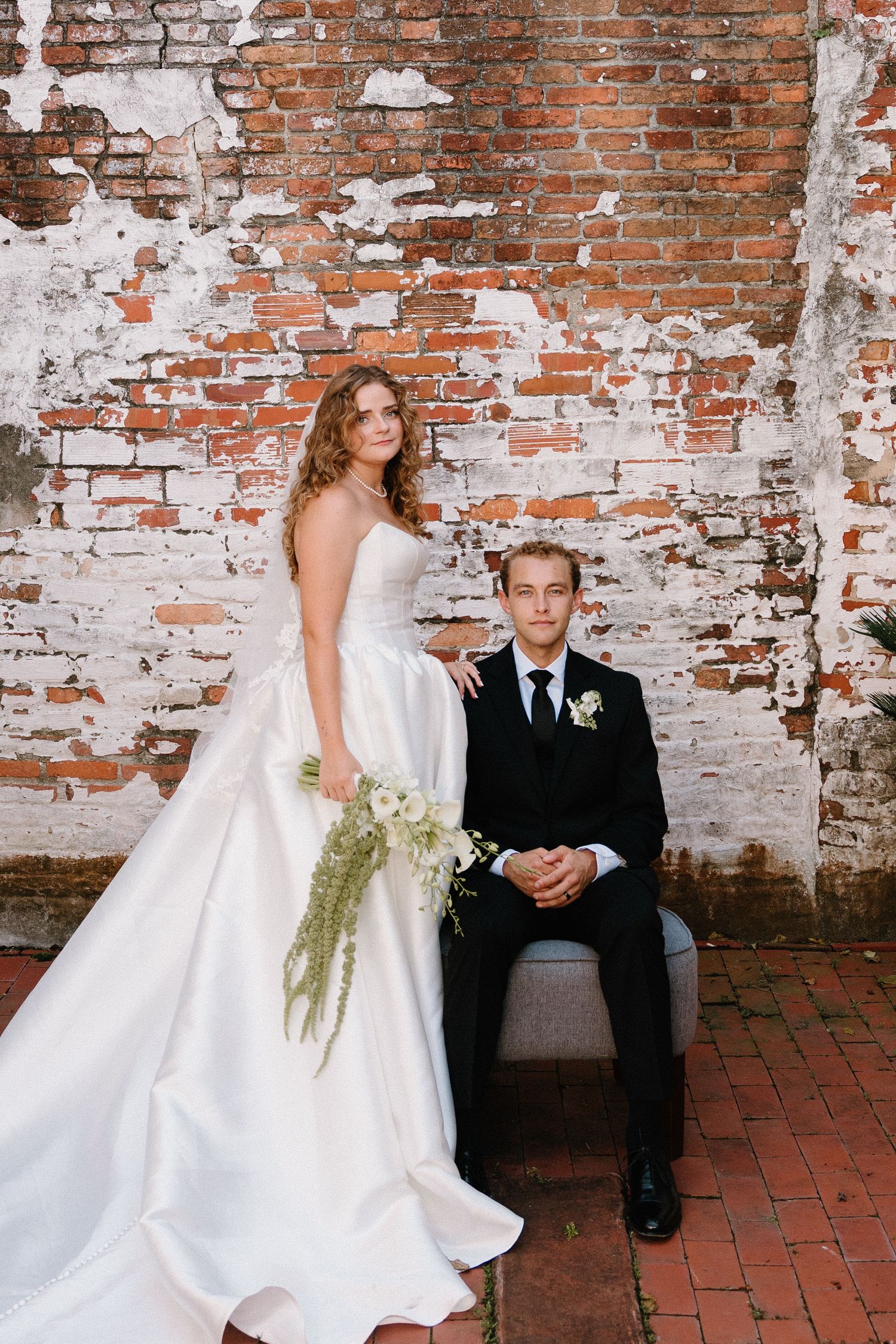 A wedding couple poses against a rustic exposed brick wall on red brick flooring in an industrial chic setting.