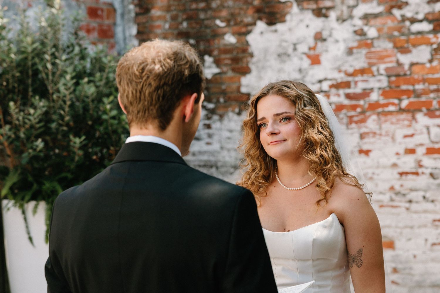 A romantic wedding couple stands against a rustic brick wall during an intimate outdoor ceremony.