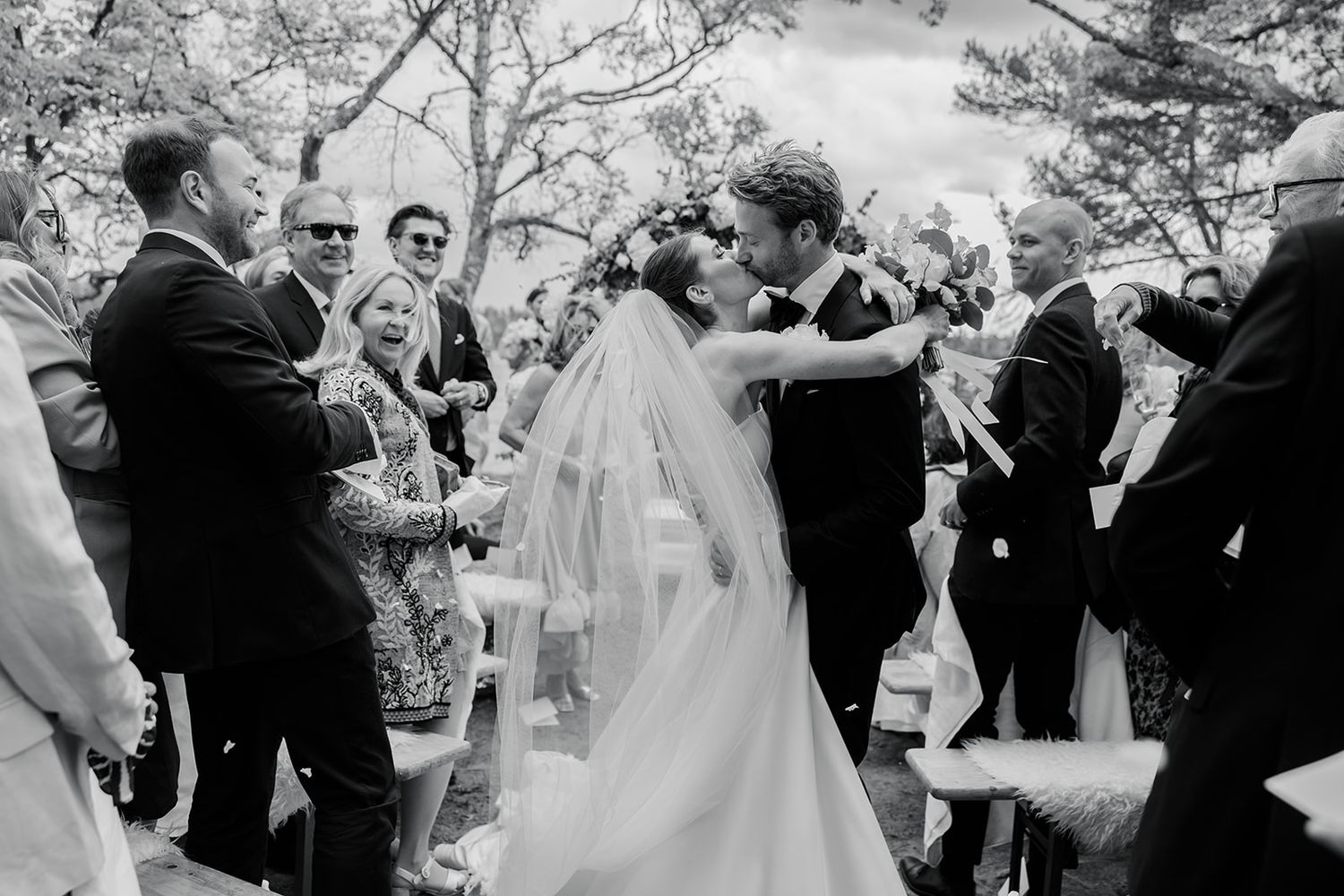 A joyful outdoor wedding ceremony moment captured in black and white as guests celebrate the newlyweds.