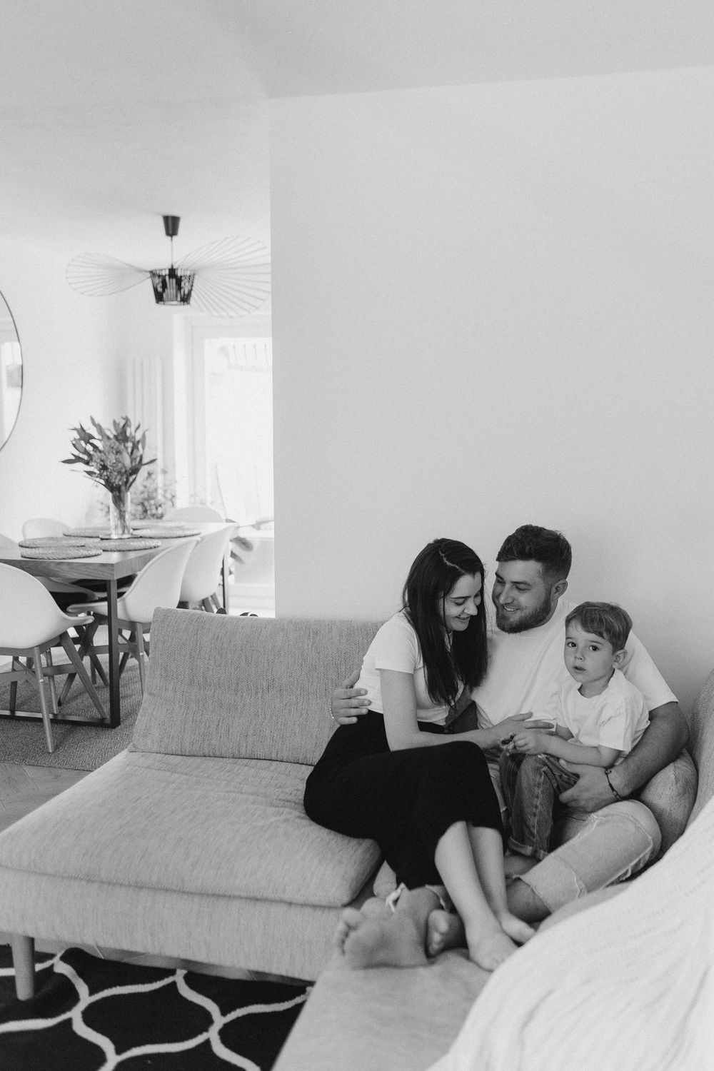Family relaxing together on a comfortable grey couch in a bright, minimalist living room.