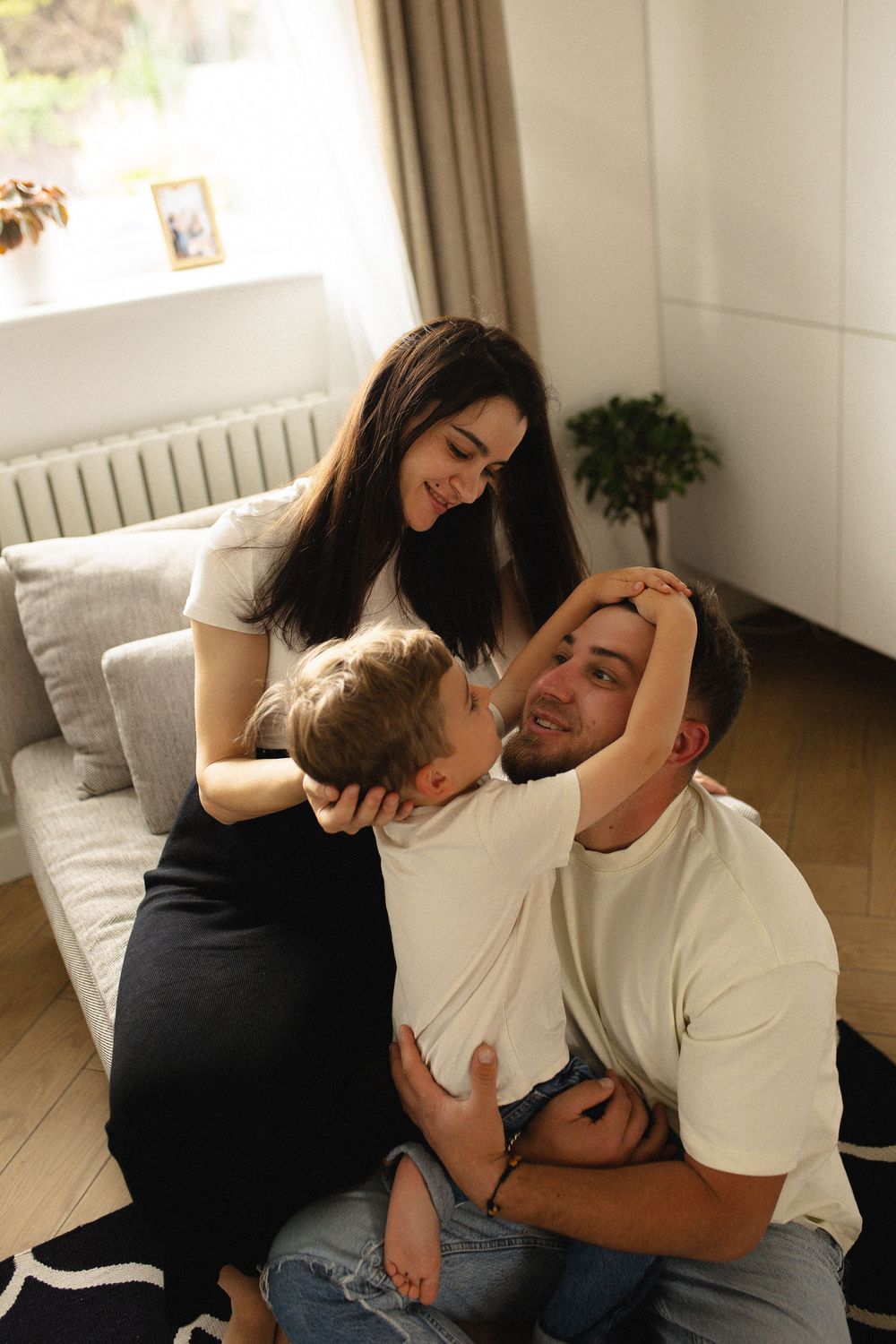 A couple shares an intimate moment while relaxing on a light gray couch in a bright living room.