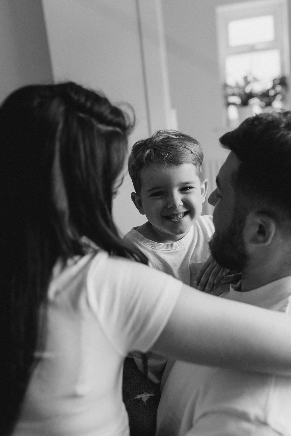 Black and white photo series showing joyful interaction between family members in a bright room.