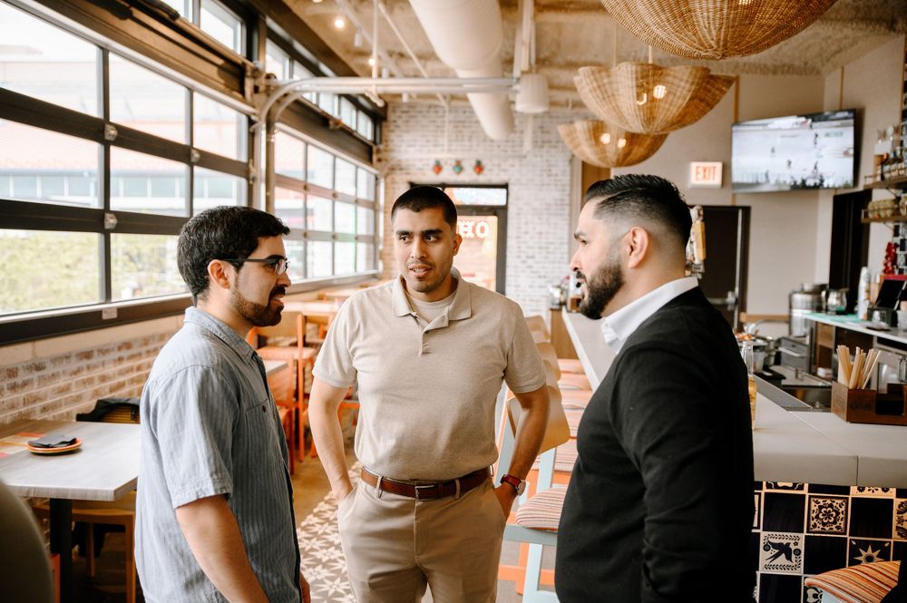 Three people having a casual business meeting in a bright industrial-style office space.