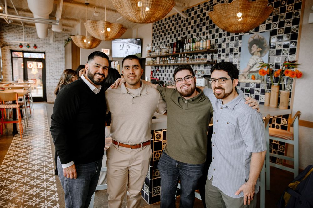 A group of people celebrate together in a modern restaurant with geometric patterned walls and pendant lighting.