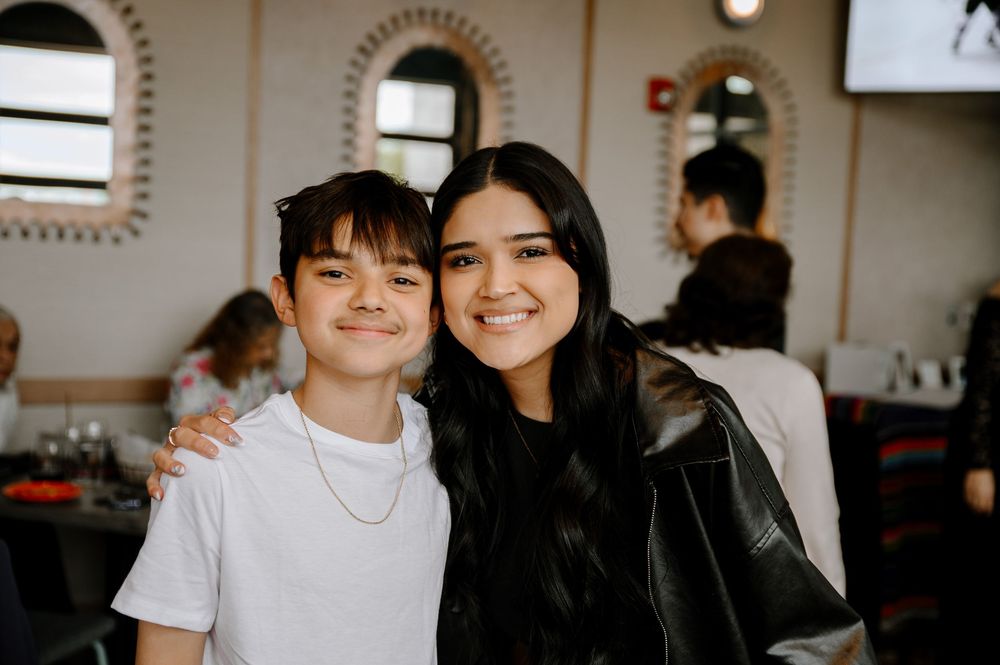 Two people sitting together and smiling in a casual indoor setting with warm lighting.