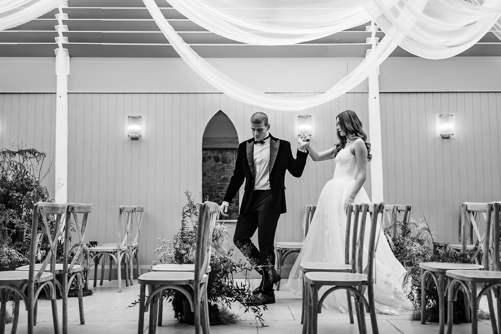 A black and white photo of newlyweds joyfully walking down the aisle at their wedding reception.