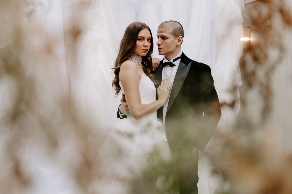 An intimate wedding portrait captured through soft focus foliage in an elegant white venue.