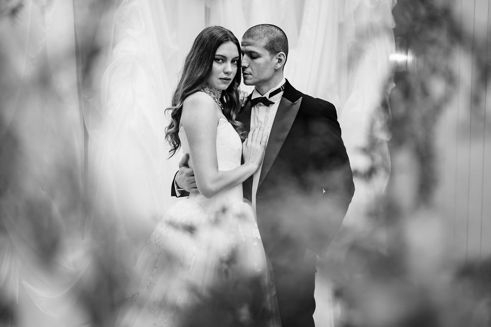 A romantic black and white wedding photo of a couple embracing through soft blurred foliage.