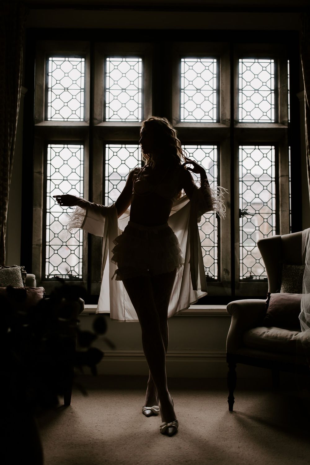 A silhouetted figure dances gracefully in front of ornate windows creating a dramatic backlit scene in a dimly lit room.