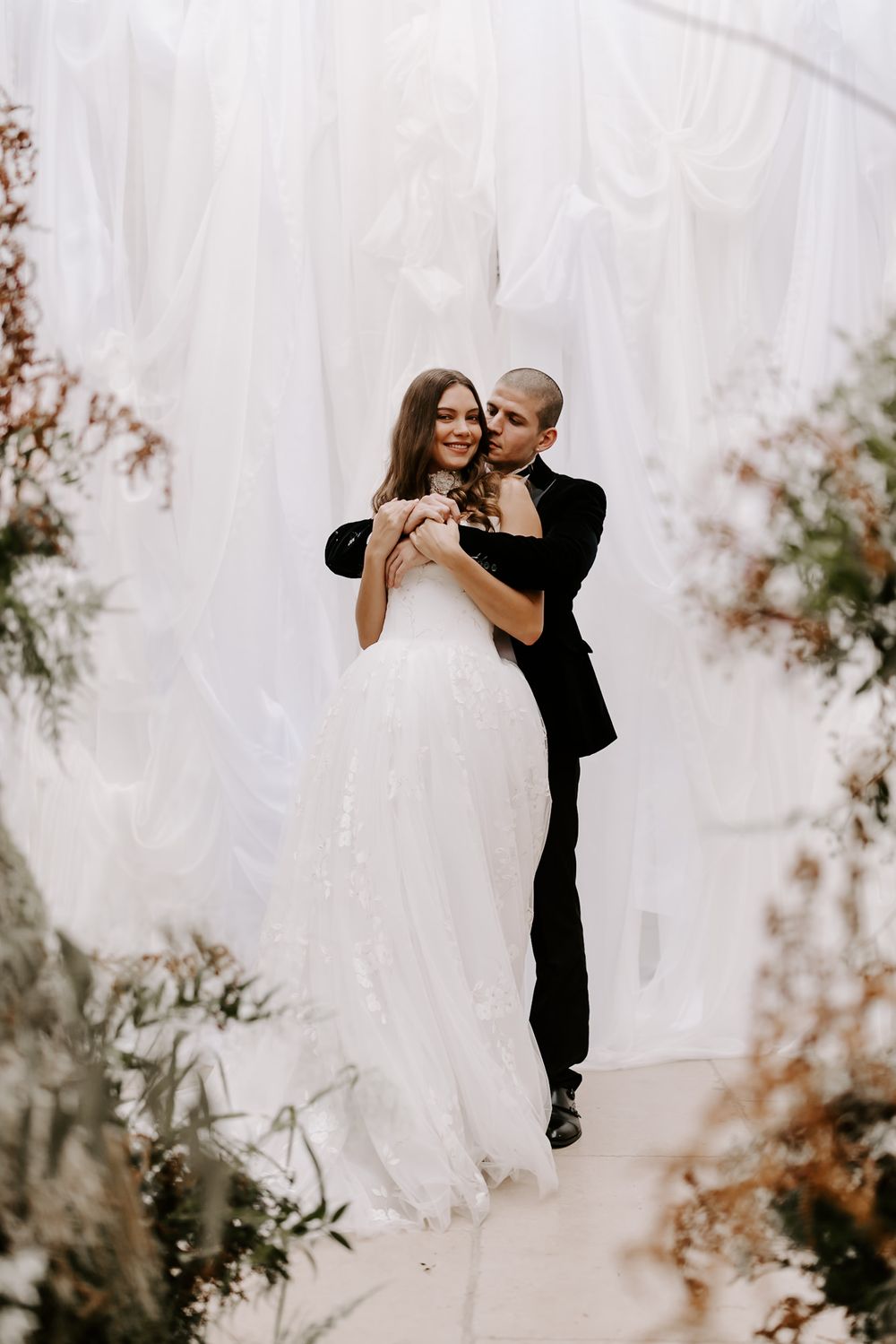 A couple in wedding attire shares a romantic dance pose against a light, ethereal background.