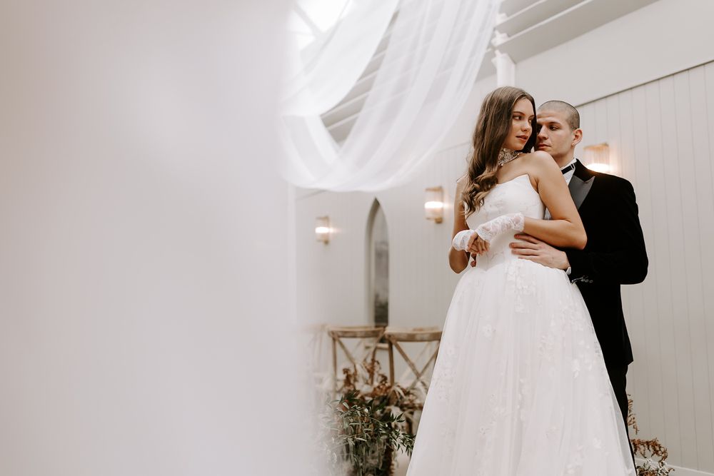Elegant bride and groom share a romantic dance together in a bright white venue during their wedding celebration.