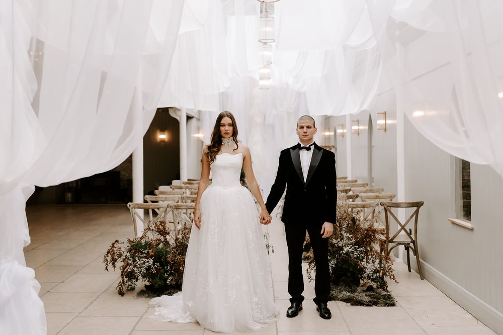 Elegant wedding party walking through white curtain-draped hallway in formal attire at upscale venue.