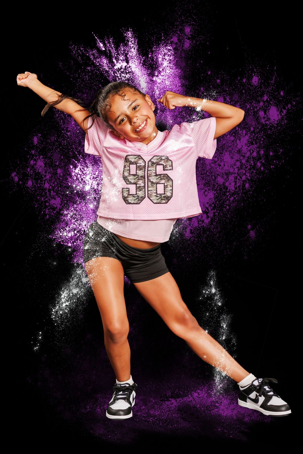 Young girl in pink jersey number 96 dancing energetically against black background with purple powder explosion.