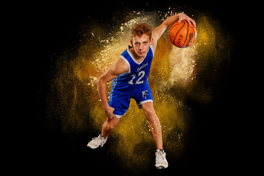 A basketball player dribbling against a golden powder explosion effect.