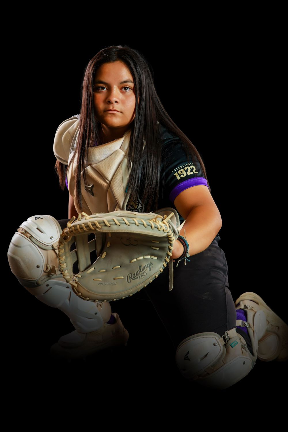 Softball player in black shirt and white turtleneck poses with catcher's mitt against dark background.