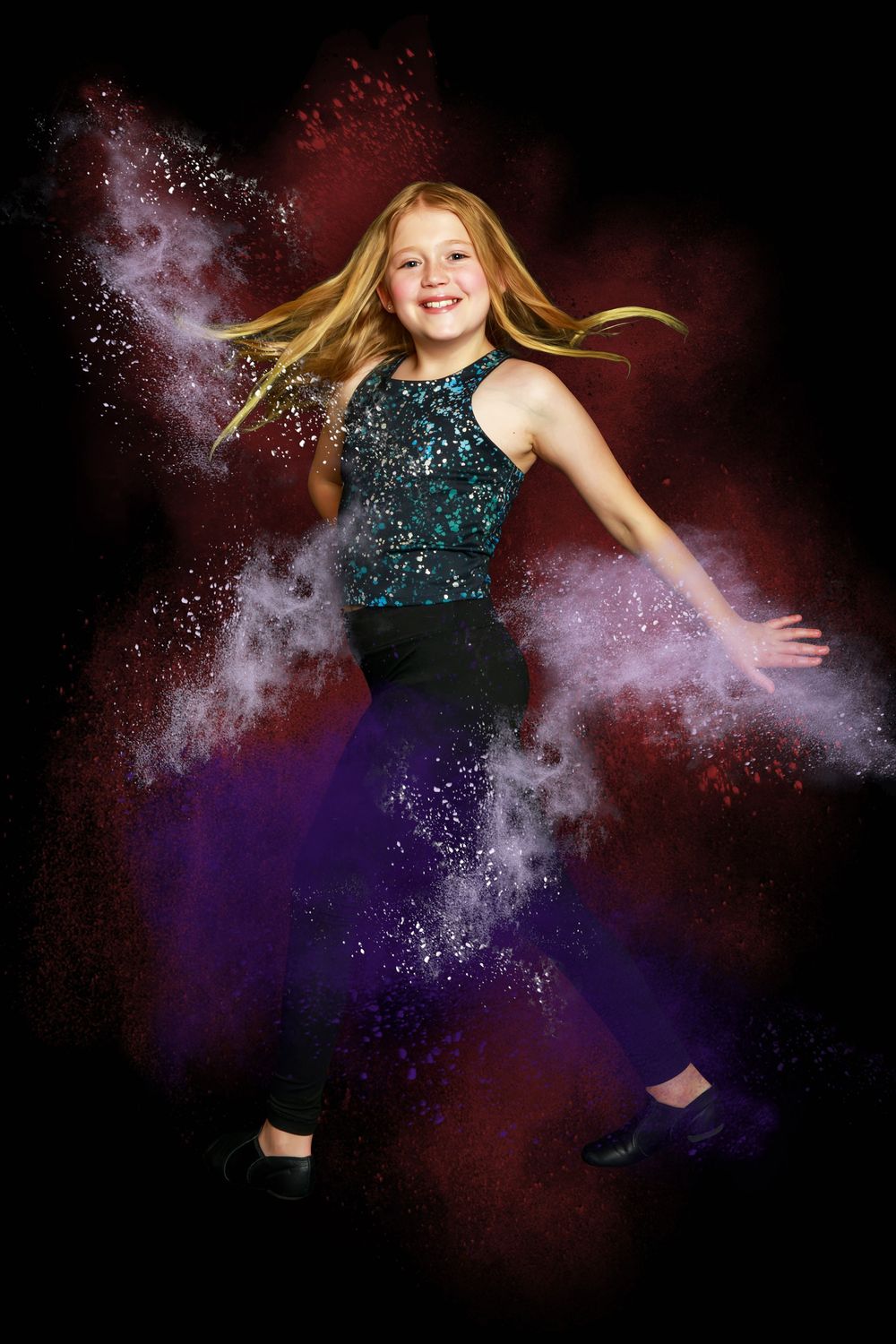 Dancer in sparkly teal top and purple pants leaps through colorful powder explosion effect against dark background.