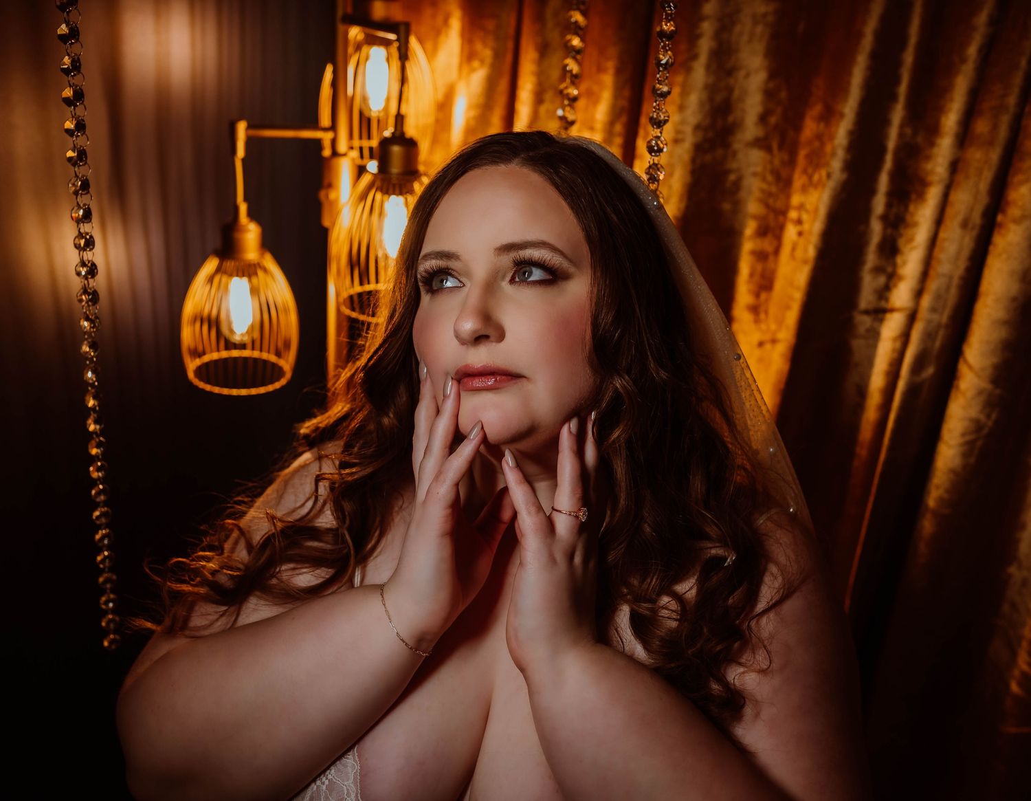 A woman in a golden-lit setting poses elegantly with warm lighting of boudoir photography creating a moody atmosphere.