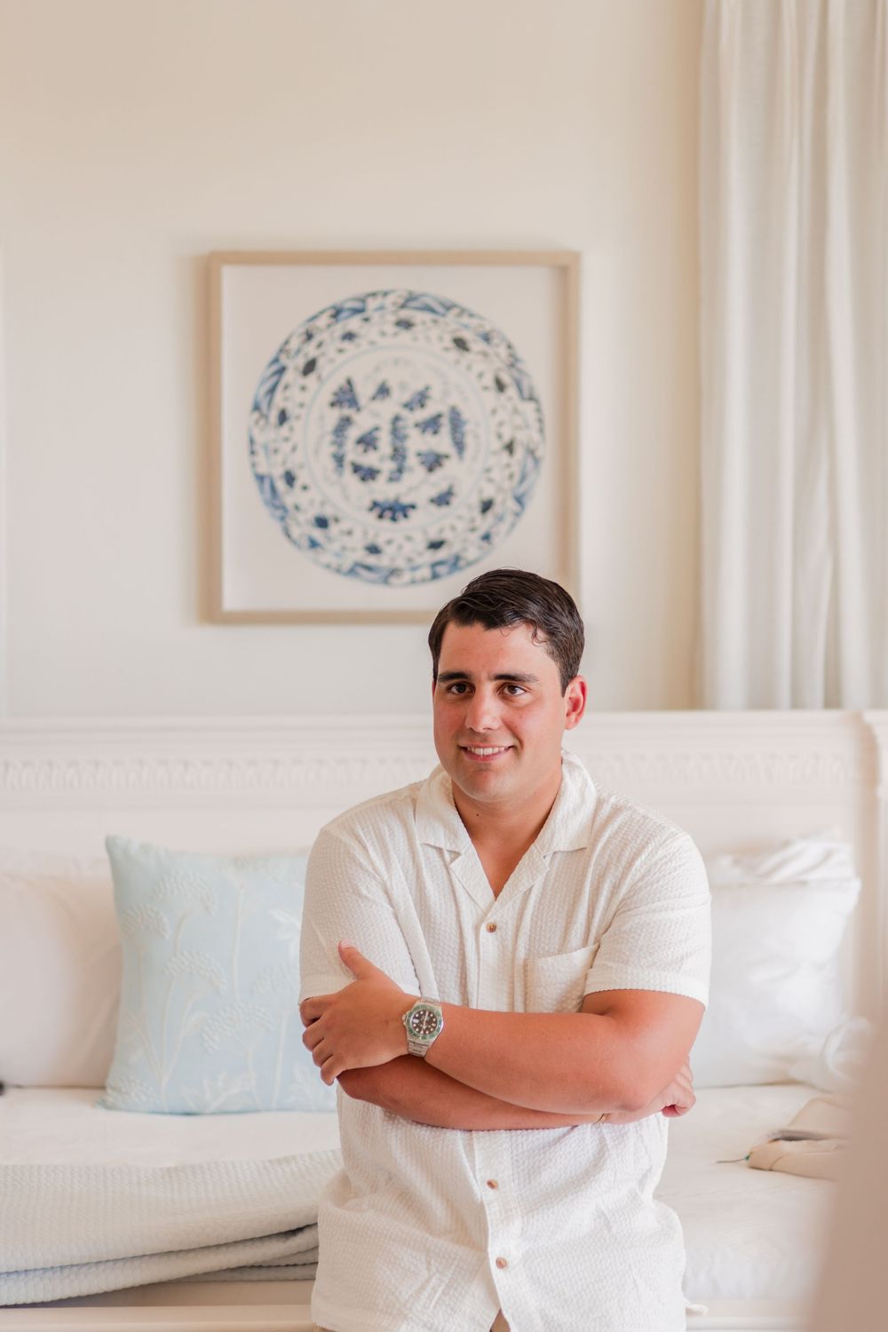 Person in white shirt sitting on white couch in bright minimalist room with framed artwork on wall.