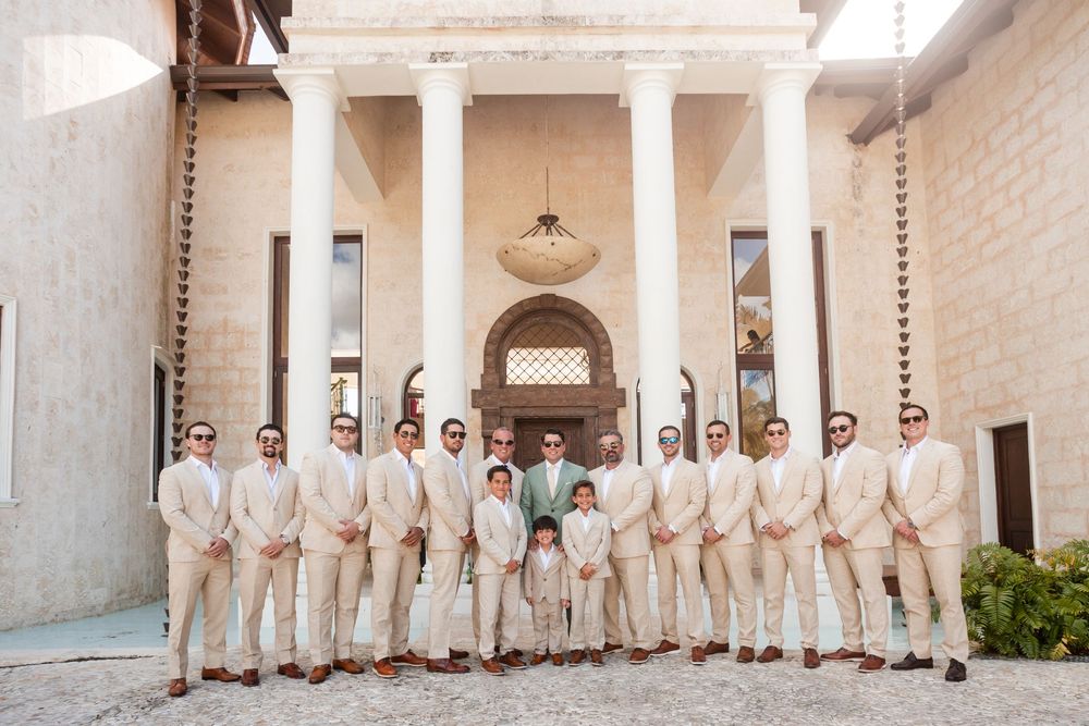Wedding party in cream colored attire poses together in a grand columned courtyard with elegant architecture.