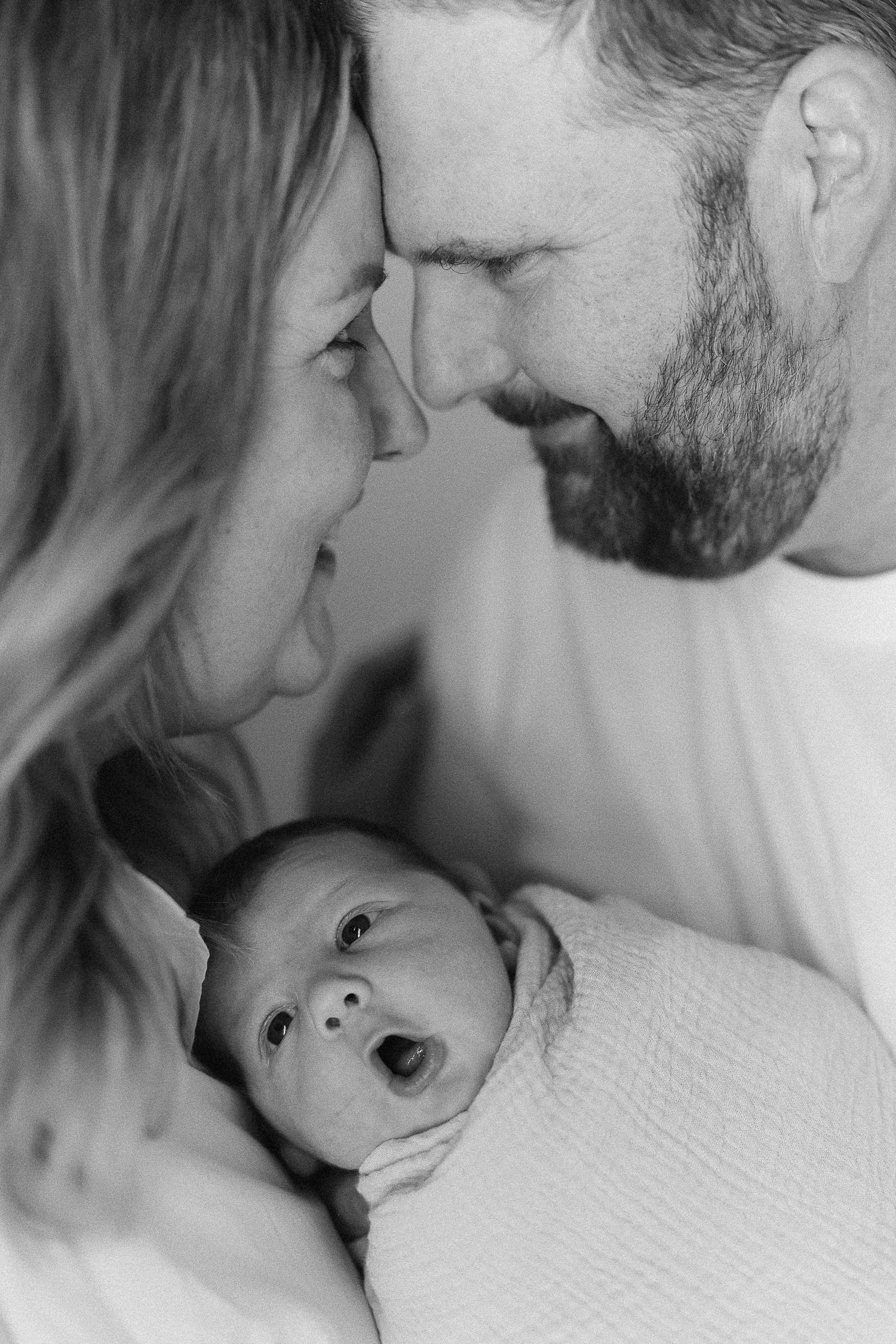 Family newborn photos with mom, dad, and baby cuddled together during a cozy studio session