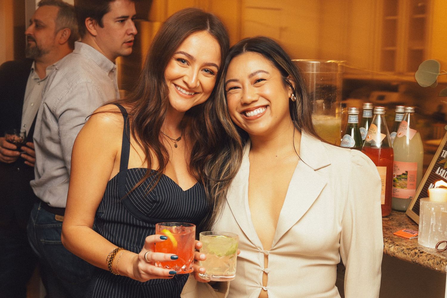 Group of friends enjoying colorful cocktails and conversation at a warmly lit bar or restaurant.