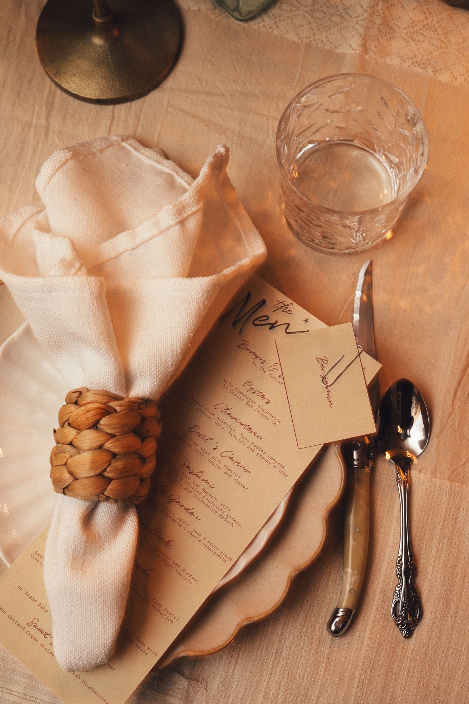 Elegant table setting with woven napkin ring, cream napkin, vintage silverware and crystal glass on wooden surface.