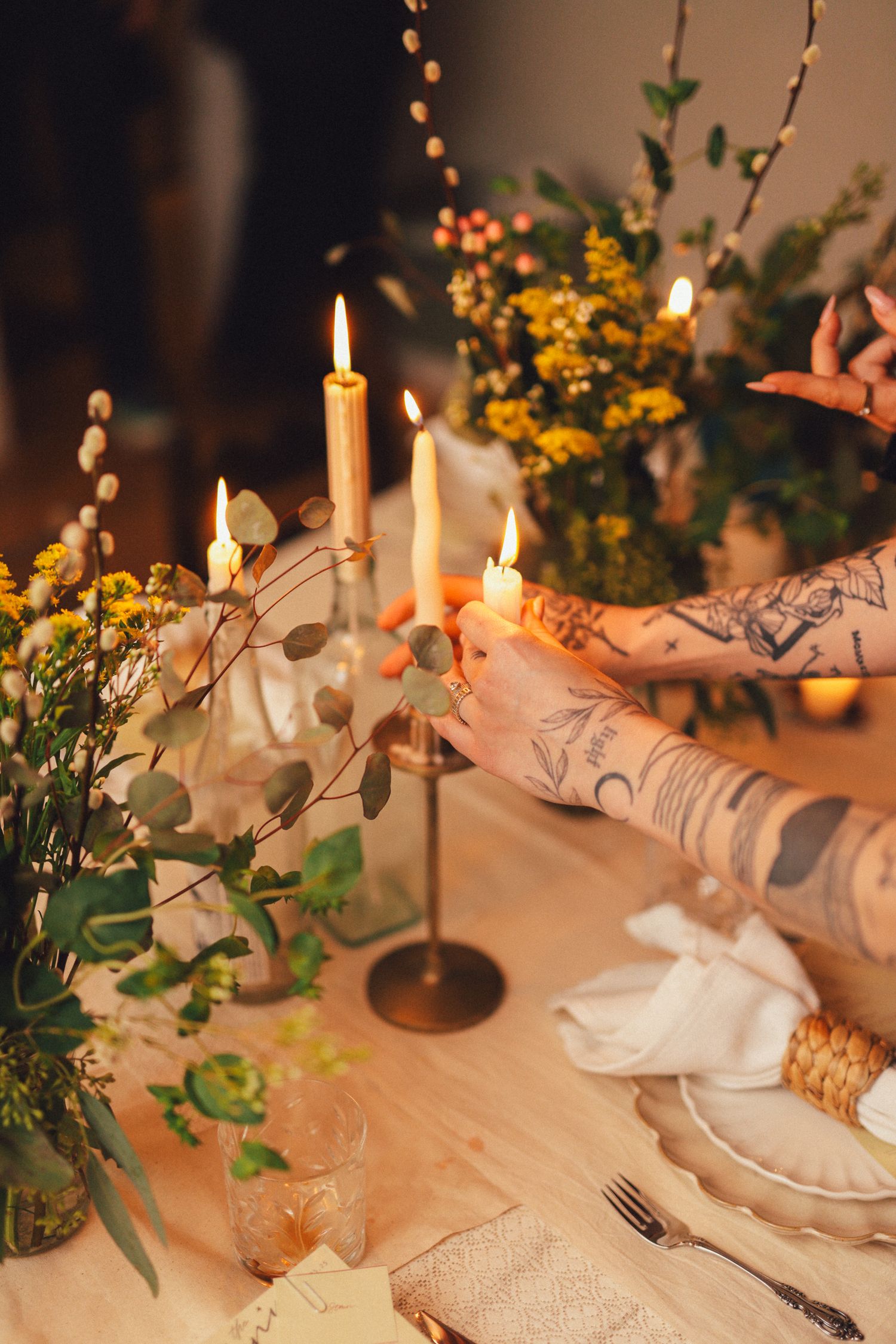 Elegant table setting with lit candles, white linens, and delicate yellow floral arrangements creating a romantic ambiance.