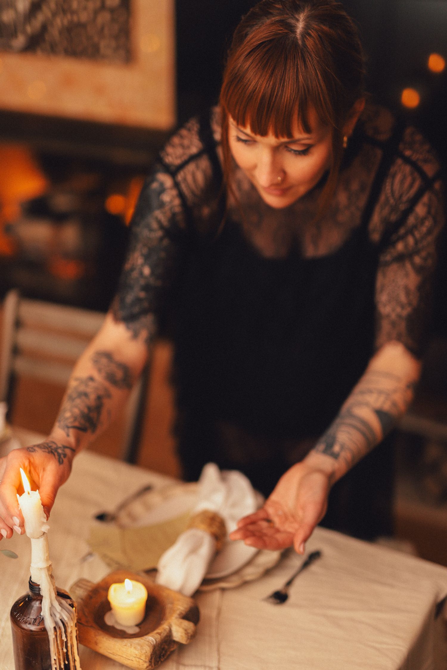 Person in dark clothing lighting candles on a white table in warm, ambient lighting.