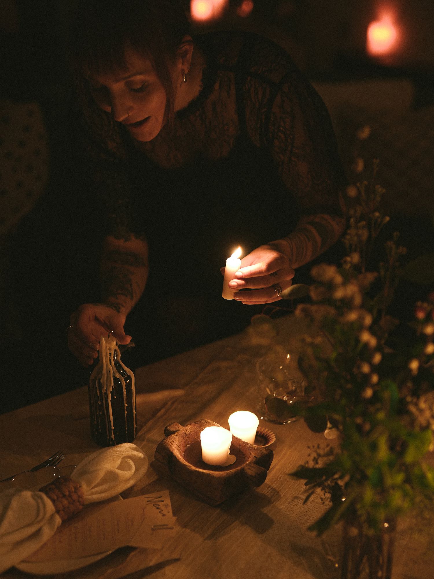 A moody candlelit table setting with glowing candles and greenery creates an intimate atmosphere in dark lighting.