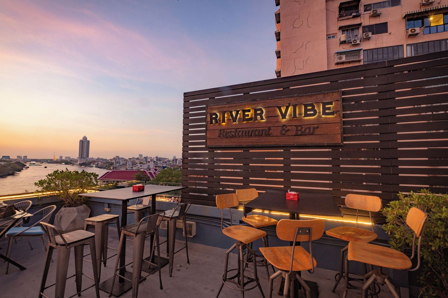 Modern restaurant booth with leather seating, purple mosaic tiles, and waterfront views through large windows.