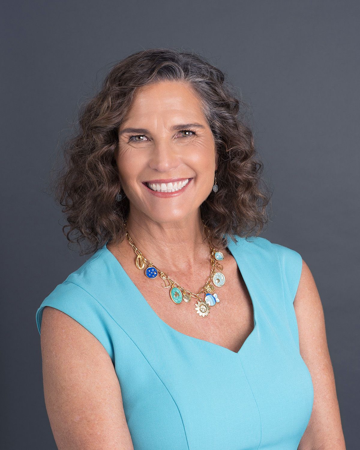 Professional headshot series of someone wearing a turquoise sleeveless top and statement necklace against a dark background.