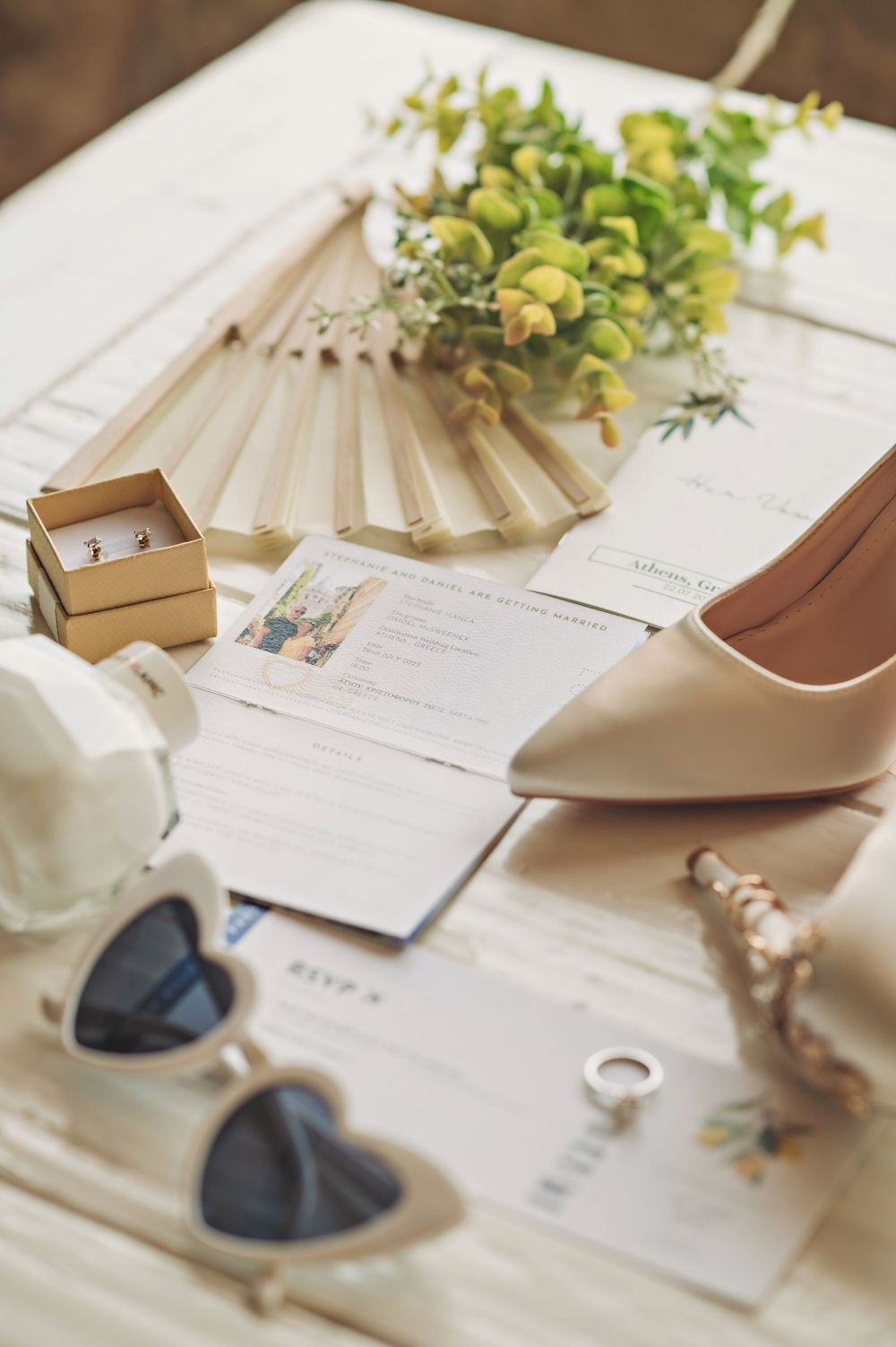 Wedding accessories including white heels, heart-shaped sunglasses and floral details arranged on a white surface.