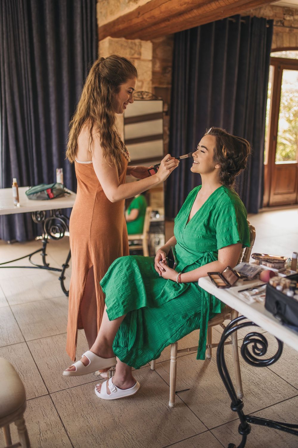Pre-wedding makeup session in a rustic venue with stone walls and dark curtains.