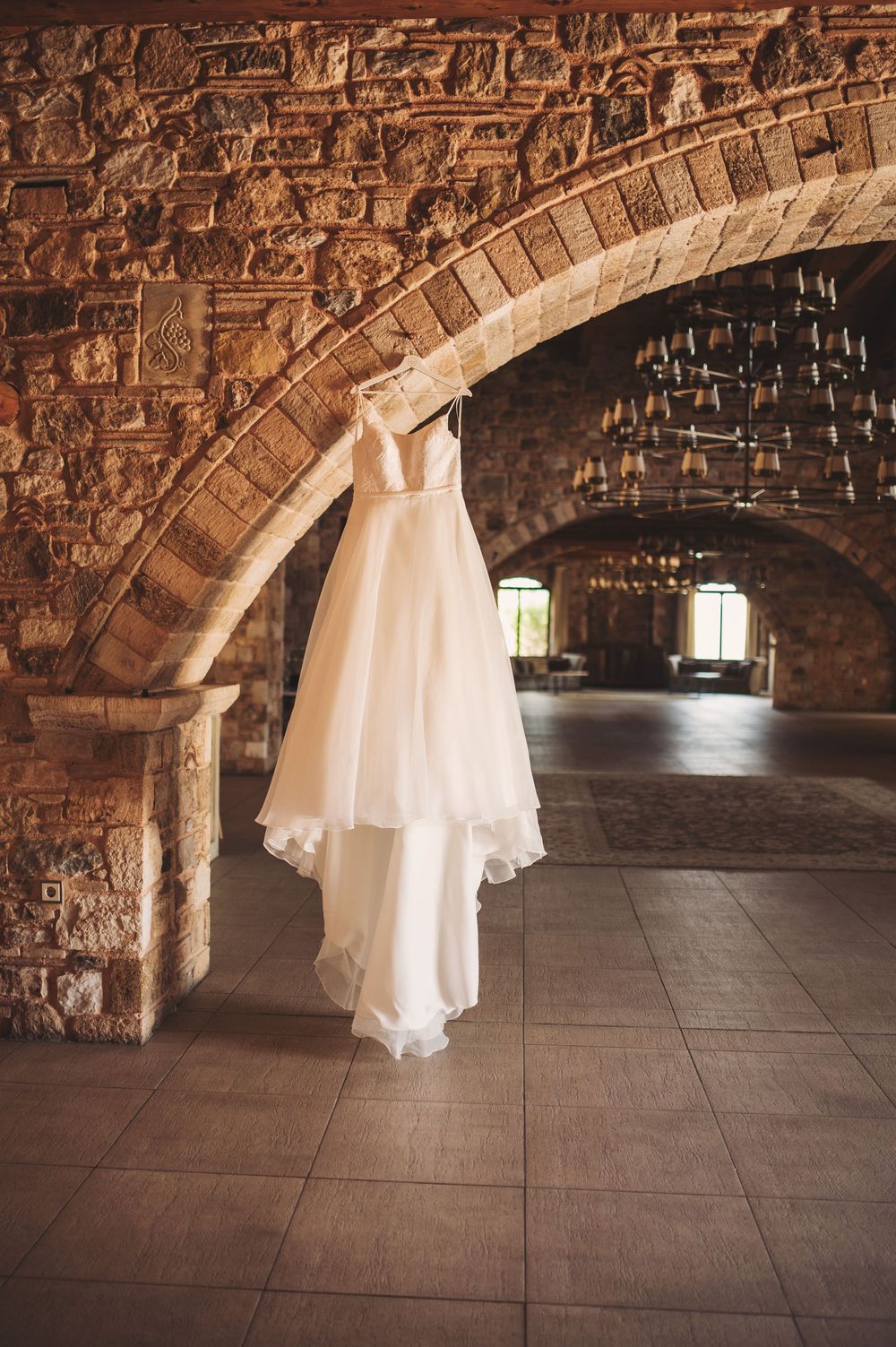 An elegant white wedding dress hangs beneath a stone archway in a historic venue.
