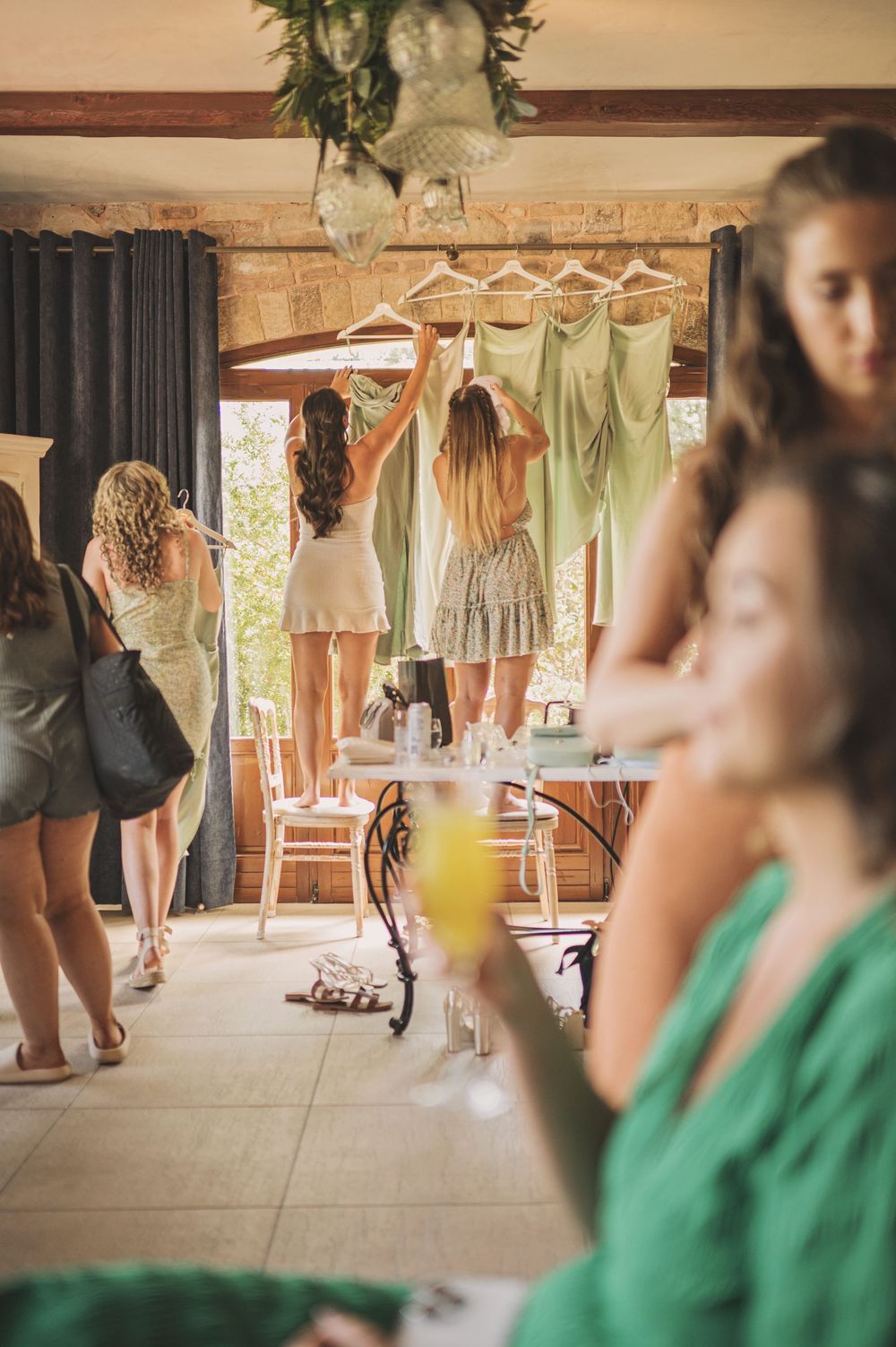 Bridesmaids' dresses hang on display while wedding party members prepare in the background.