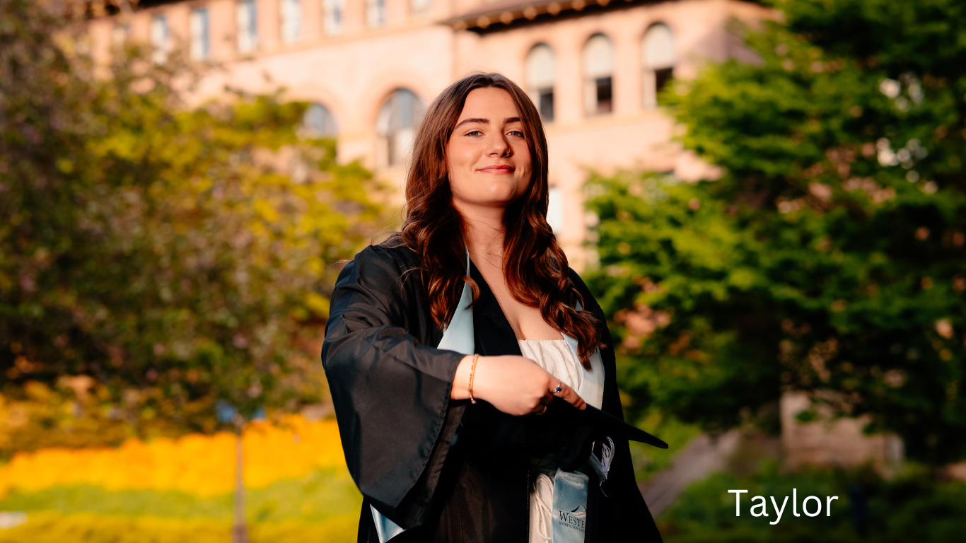 Graduate in black academic regalia smiling outdoors with historic building in background.