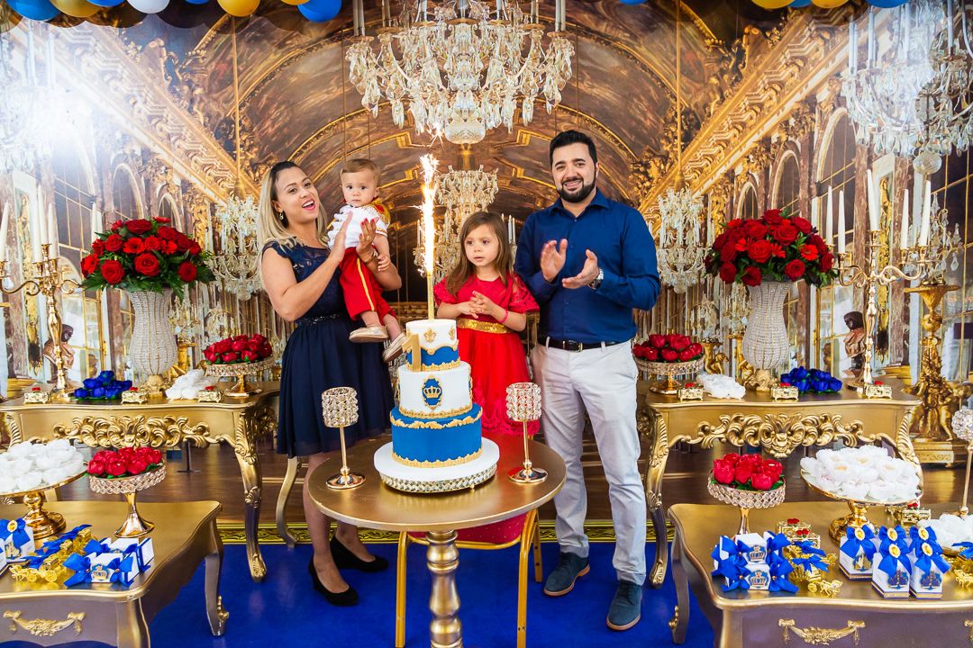 Luxurious birthday party setup with ornate chandelier, gold decor, and red and blue dessert display on elegant table.
