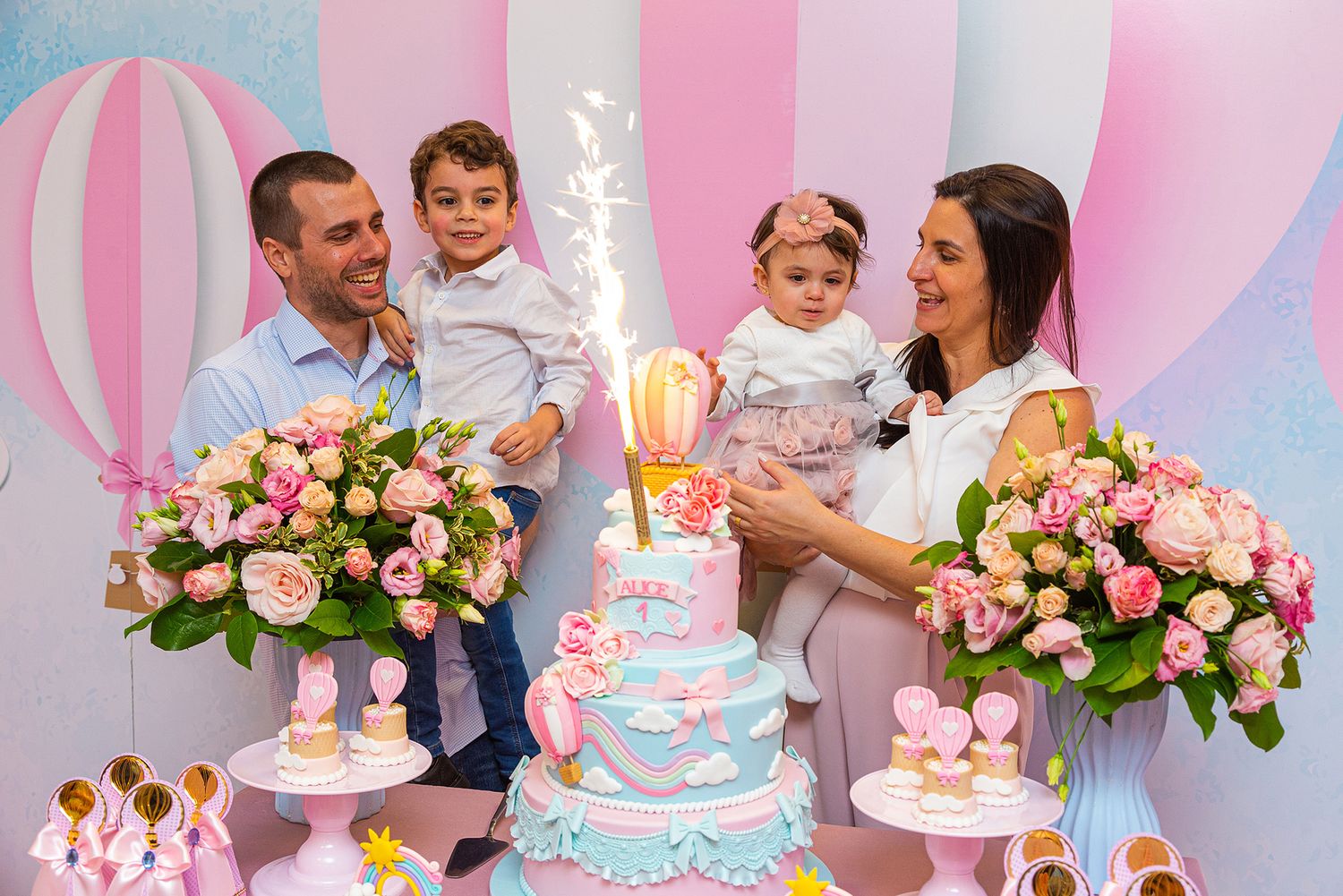 Hot air balloon themed first birthday party celebration with blue and pink decor, floral arrangements and tiered cake.