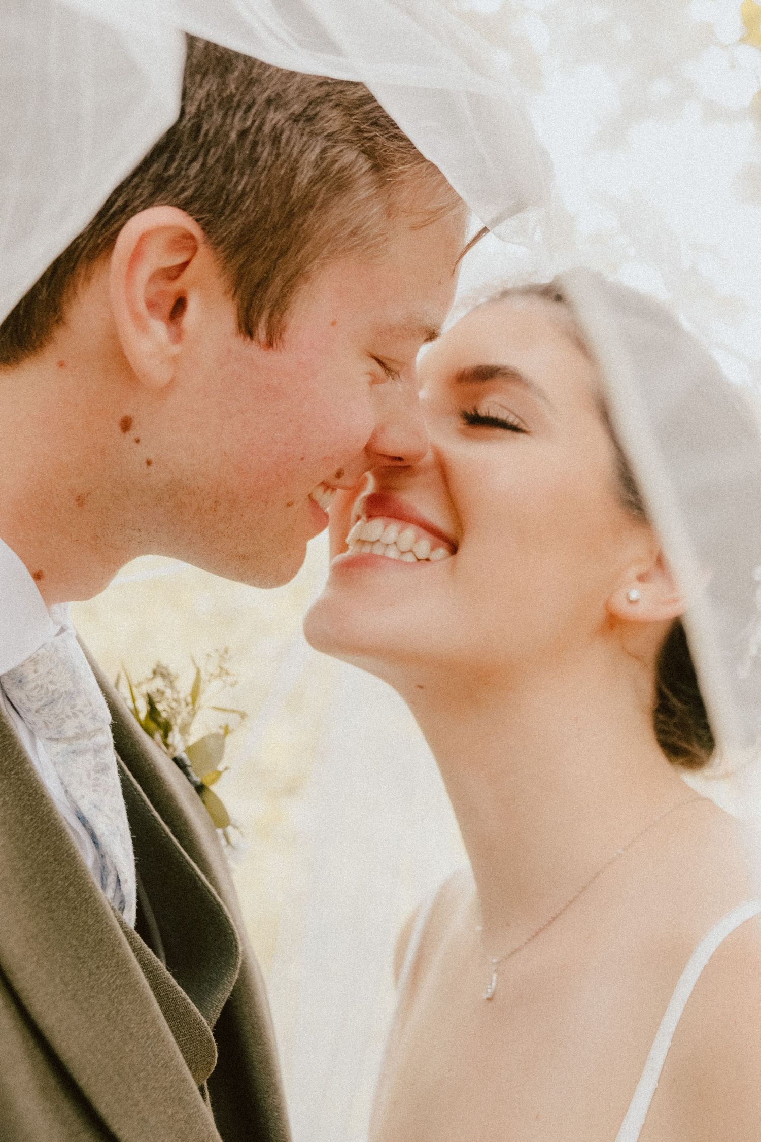 Close-up of newlyweds sharing intimate moment under bridal veil.
